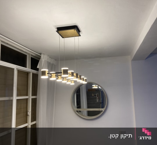 סלון מעוצב עם גוף תאורה תלוי, מראה עגולה על הקיר ואיזור חלון מודרני